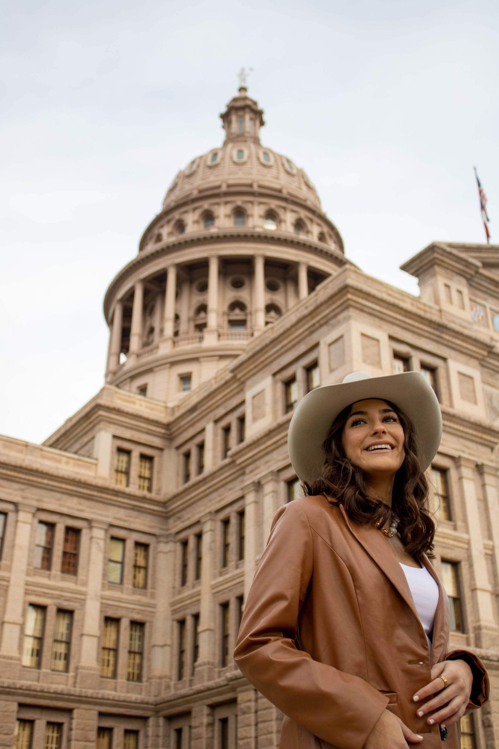 College girl in a cowboy hat smiling in front of the Texas Capitol building