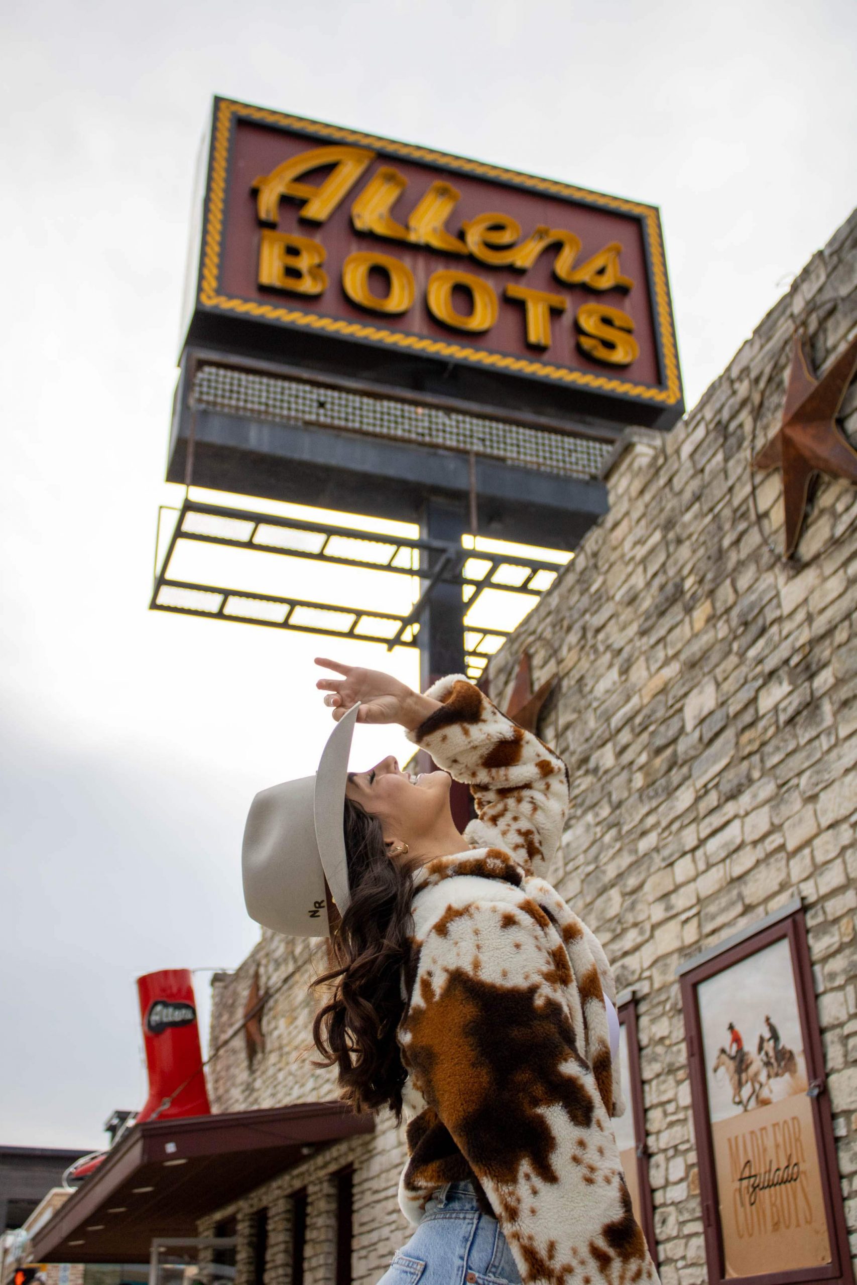 College student tipping her cowboy hat backwards in front of the South Congress Allen's Boots sign