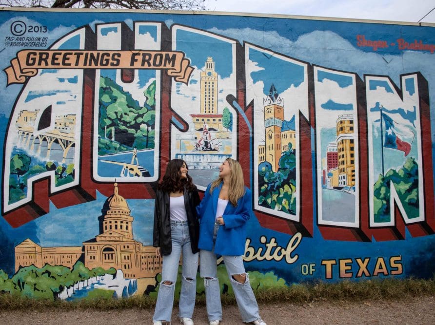 Two girls laughing in front of the Greeting from Austin Mural on South Congress