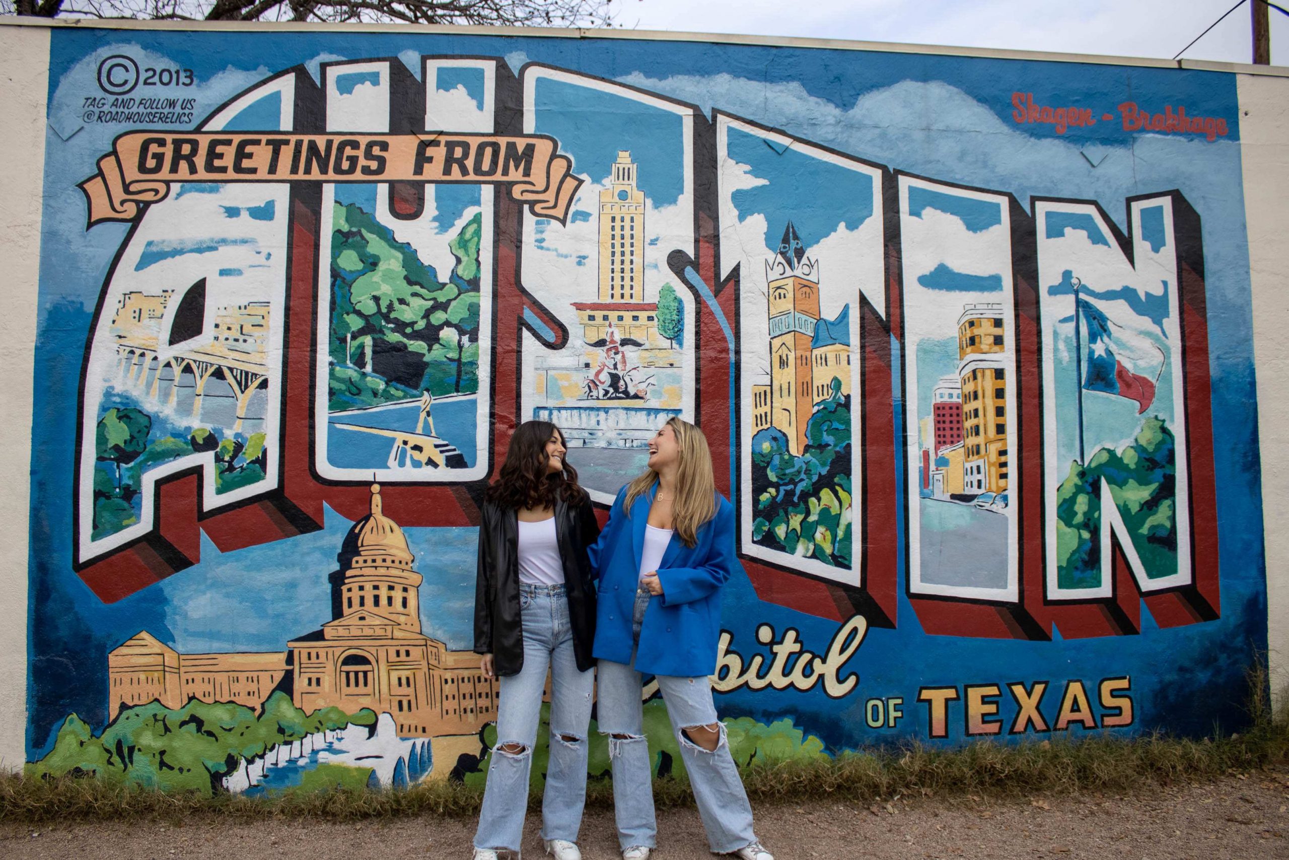 Two girls laughing in front of the Greeting from Austin Mural on South Congress
