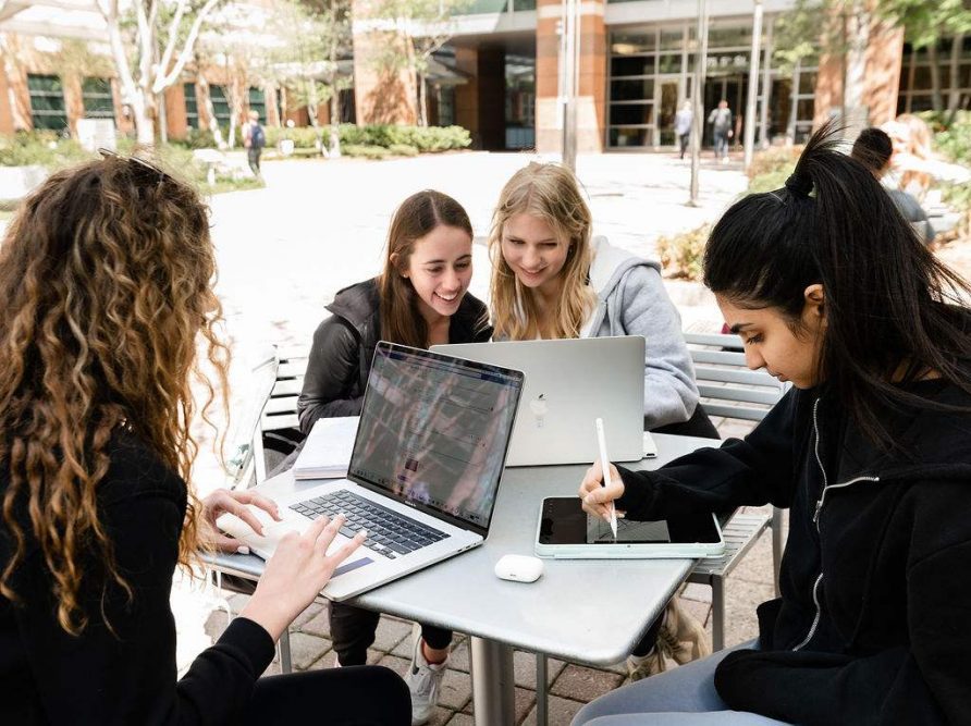 Four college girls studying together at an outdoor table on campus