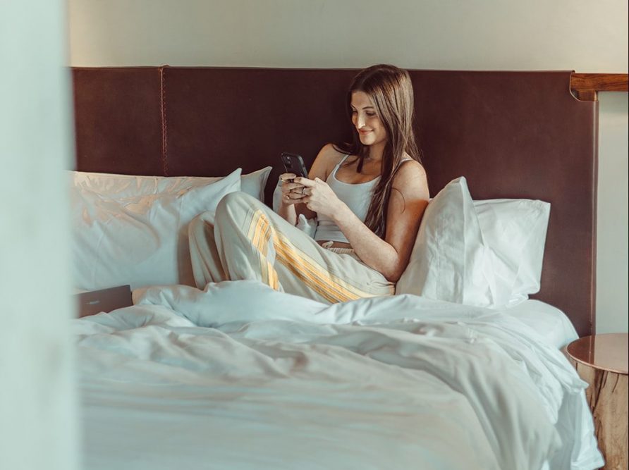 A girl smiles while texting her friends from her bed in her brand new apartment