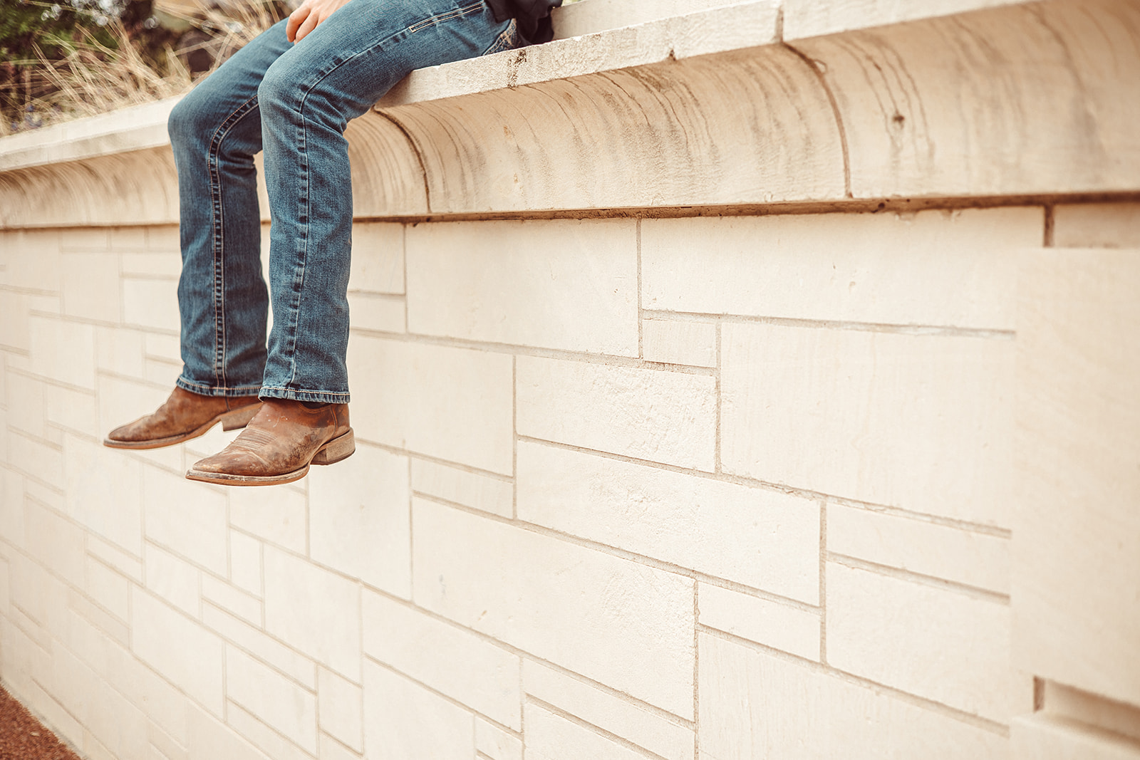 A student's cowboy boots and jeans dangle off a stone ledge on the UT Austin campus