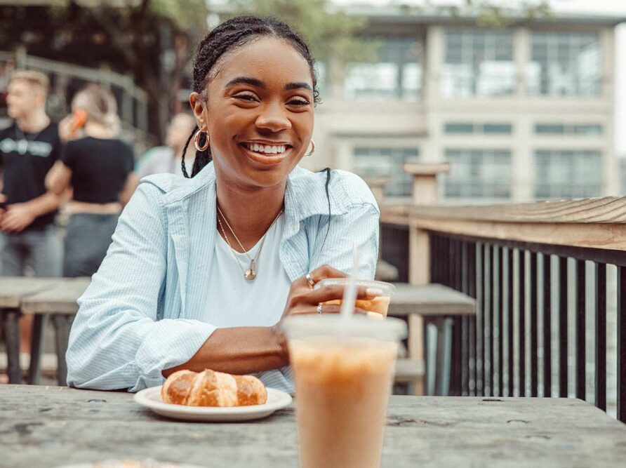 UT Austin student enjoys a pastry and iced coffee from Mozart's Coffee Roasters while sitting on the deck overlooking Lake Austin.